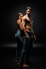 Fototapeta na wymiar attractive woman touching jeans of muscular man on black