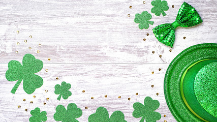 Happy Saint Patrick's Day greeting card with traditional symbols, shamrock, green attire. Green hat, bow tie, St Patricks Day shamrocks, golden confetti on white wooden background, copy space