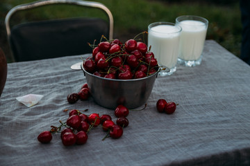 sweet cherries and two glasses of milk stand on a table on a street in a village