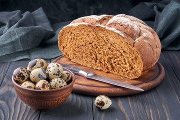 Pumpernickel - bread made with a combination of rye flour and whole rye grains. Quail eggs in a clay bowl, bread knife. Fresh healthy farm food.