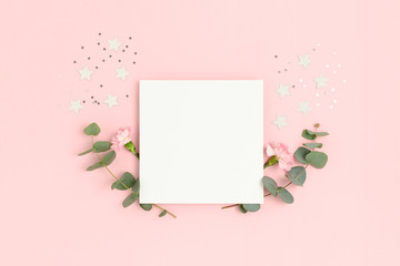 Blank paper card mockup with carnation flowers, eucalyptus and stars confetti. Holiday concept with place for text on a pink pastel background.