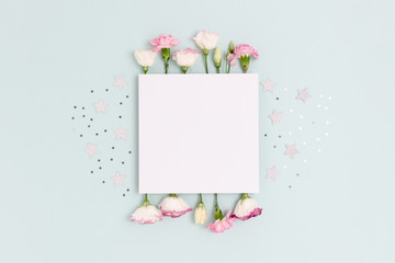 Blank paper card mockup with eustoma, carnation flowers and stars confetti. Festive concept with place for text on a blue pastel background.