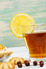 Cup of hot tea with lemon and cookies on a white wooden background.