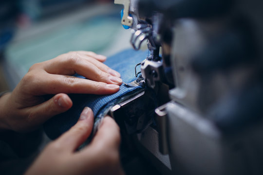 Young beautiful seamstress sews on sewing machine in factory