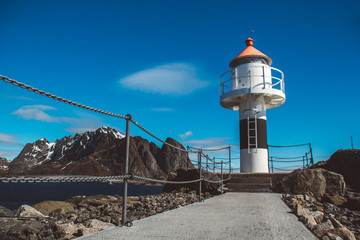 Fototapeta na wymiar Lighthouse on the pier on the background of the mountains and the blue sky on the Lofoten Islands. Place for text or advertising