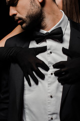 young woman in gloves hugging man in suit isolated on black