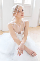 Blonde girl is sitting on the floor in a beautiful white wedding dress. A woman bride is waiting for the groom before the wedding