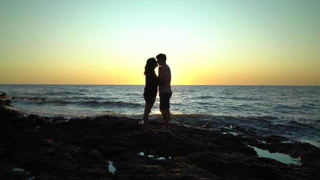 Silhouette of couple kissing on rocks on the beach