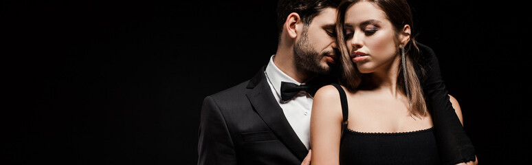 panoramic shot of handsome man in suit near beautiful woman in glove isolated on black