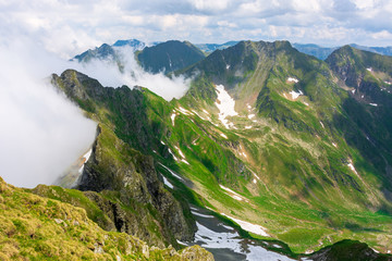 Fototapeta na wymiar great summer scenery of high mountain range. steep slopes with rocks, grass and spots of snow. clouds on the blue sky. explore fagaras ridge of romania travel concept