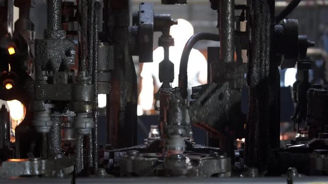 Automated process of forming a bottle of molten glass. The molten glass mass enters the mold and then into the glass blower where the bottle is formed. Production of glass bottles.