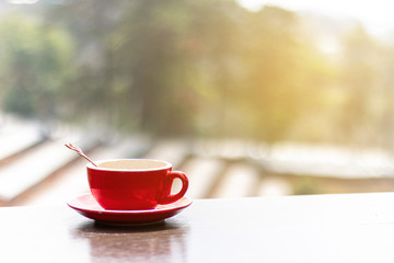 Red hot coffee mug on a wooden table with natural background blurred in the morning.