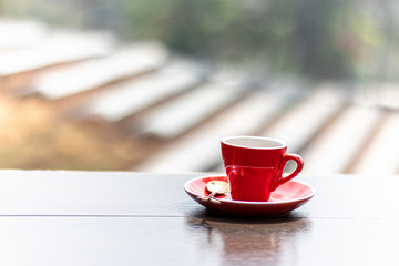 Red hot coffee mug on a wooden table with natural background blurred in the morning.