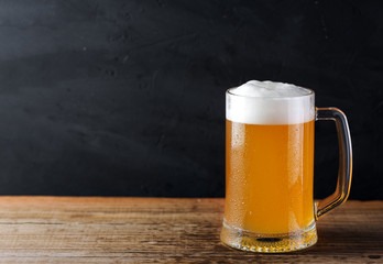 A mug of foamy light wheat beer on a wooden table copy space