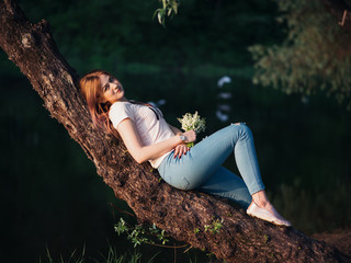 Beautiful young woman with a bouquet of spring flowers on the river Bank near a tree