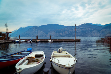 Fototapeta na wymiar Boat in Lake Garda Italy in cold foggy day in winter holidays with city historical view, lake and mountain and cable car 