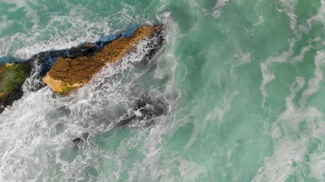 Super slow motion of sea waves crushing on surface rocks, aerial overhead view