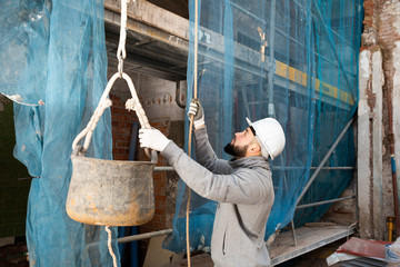 Man raising bucket with construction mortar on rope