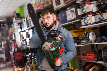 Fototapeta na wymiar Positive male is buying new chainsaw