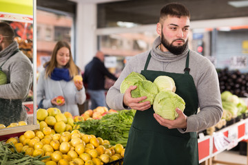 Male shop assistant in an apron carries fresh cabbage