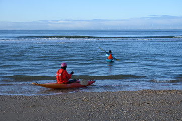 Unidentified people in kayaks going in to water on North sea sandy beach during low tide near...