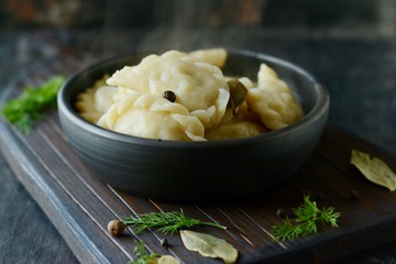 Dumplings with potatoes with herbs, spices and butterin a ceramic bowl on a dark background. Varenyky, vareniki, pierogi, pyrohy - dumplings with filling.