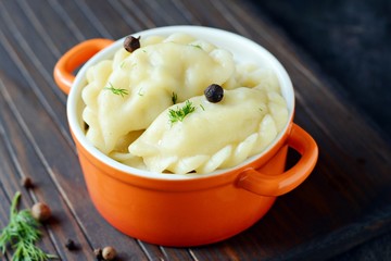 Dumplings with potatoes with herbs, spices and butter in a ceramic portion pot on a dark background. Varenyky, vareniki, pierogi, pyrohy - dumplings with filling.