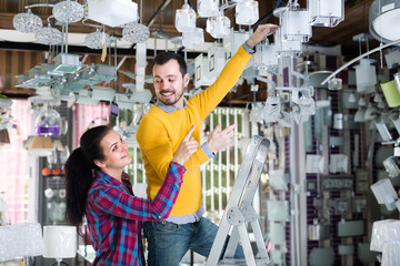 Obraz na płótnie Canvas Man and woman are choosing stylish and modern chandelier lamp.