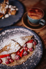 Shrove Tuesday, Pancake Day. Delicious pancakes served with fresh strawberries, vanilla ice cream and icing sugar. Cup of coffee in the background. Concept of English traditions and food.