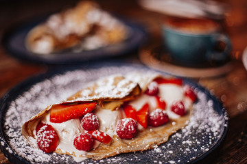 Shrove Tuesday, Pancake Day. Delicious pancakes served with fresh strawberries, vanilla ice cream and icing sugar. Cup of coffee in the background. Concept of English traditions and food.