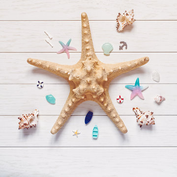 Vacation or travel planning concept. Starfish is on a white wooden background. Nearby are shells and miniature figures of boats, starfish, anchors and oars. Flat lay.