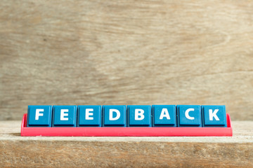Tile letter on red rack in word feedback on wood background