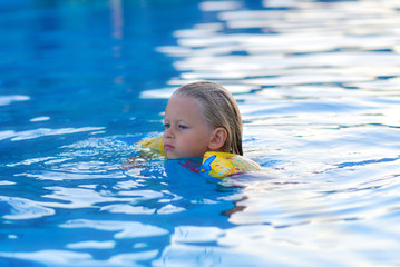 Girl in a life jacket swims in the pool