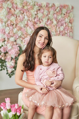 Beautiful girl with tulip flowers in hands on floral background. Greeting card for Women's Day March 8 or Mother's Day.Family mother and baby daughter with bouquet of tulips in chair,floral background