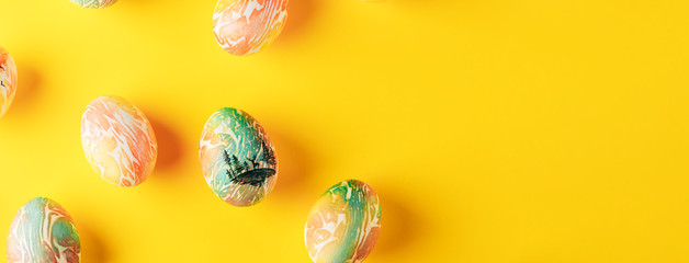 Easter eggs painted in orange and green colors on yellow background, flat lay, space for text