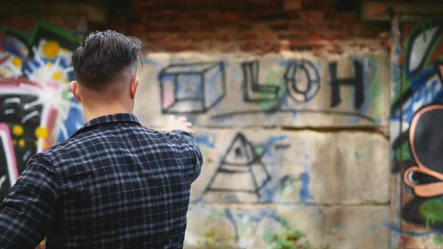 Bully guy is dressed in casual clothes, checked shirt. He is throwing a piece of brick into a graffiti background. Copy space. 4K.
