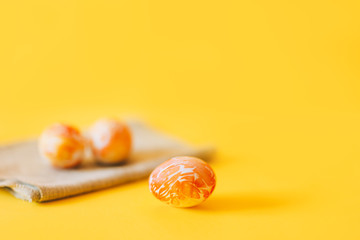 Three orange painted easter eggs, on green napkin, yellow background.
