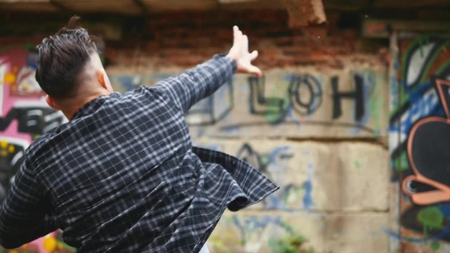 Bully guy is dressed in casual clothes, checked shirt. He is throwing a brick into a graffiti background. Slowmo. Slow motion. Copy space. 4K.