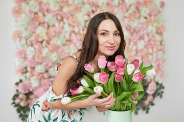 Obraz na płótnie Canvas Beautiful girl with tulip flowers in hands on floral background. Greeting card for Women's Day March 8 or Mother's Day.Very nice florist woman holding beautiful colourful blossoming flowers bouquet