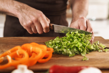 Cropped image of handsome mature man cutting ingredients for salad