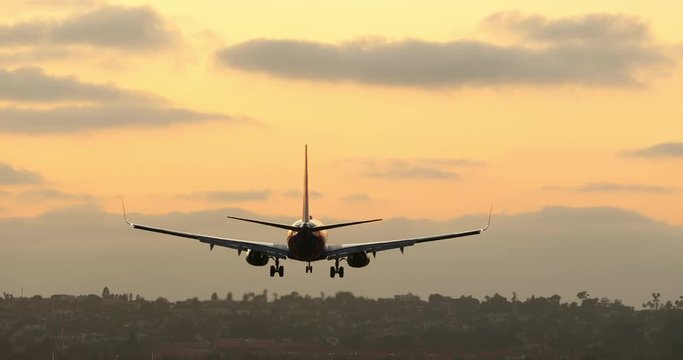 An airplane descent from the early evening sky to the wide landing strip of an airport. Many airport lights are already lit. Two other aircrafts are seen aside ready for taxiing to the runway. 4K