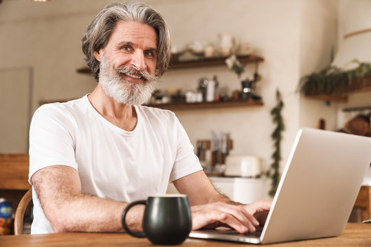 Image of smiling mature man working with laptop while sitting at table