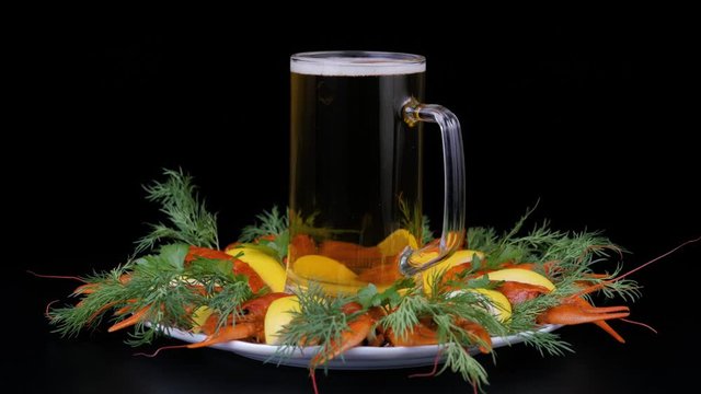 Glass of beer with foam and a boiled crawfishes. River crayfish with lemon and green-stuff rotating on a white plate. Side view.