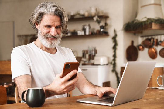 Image of smiling mature man using laptop and smartphone