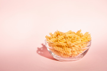 Italian pasta in glass bowl on pink backdrop with copy space