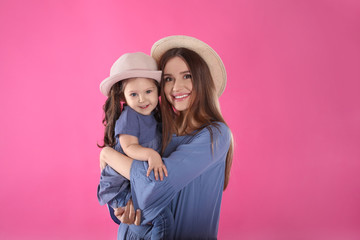 Young mother and little daughter with hats on pink background