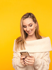 Naklejka premium Happy woman holding phone and using it isolated over the yellow studio