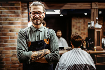 Barber man in an apron with arms crossed and happy in salon