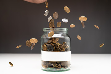 Coins in a jar with blank white label. Money falling from the sky above. Savings abstract concept. Copy space.