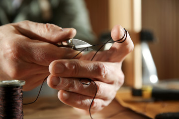 Man cutting thread while working with leather at table, closeup